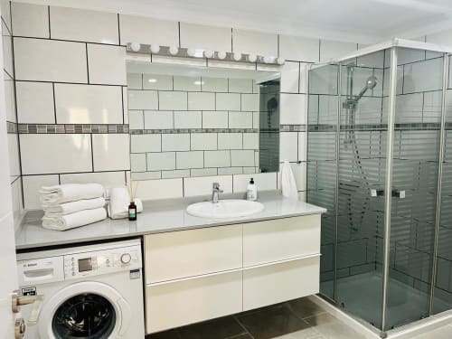 Modern bathroom in Family Suite 401 at Sunset ocean view hotel with white tiles, vanity sink, shower enclosure, and washing