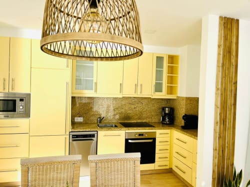 Modern yellow kitchen with granite countertop, stainless steel appliances, and woven pendant light in Sunset ocean view