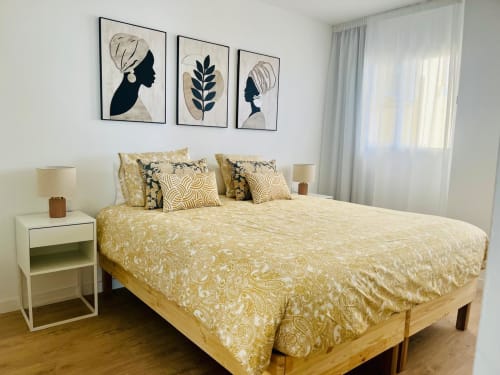 Modern bedroom in Arguineguín hotel suite with gold patterned bedding, abstract wall art, white nightstand, and ocean view