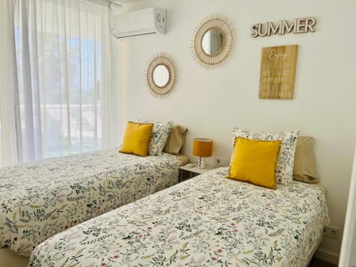 Bright twin bedroom in Arguineguín with floral bedding, yellow pillows, woven mirrors, and summer decor in family suite