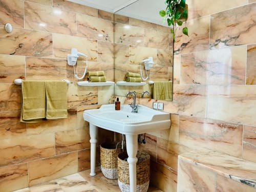 Modern bathroom in Sunset ocean view hotel suite with marble-look tiles, pedestal sink, and golden towels in Arguineguín.