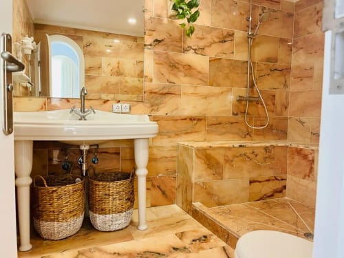 Luxury bathroom in Sunset ocean view suite with marble tiles, modern shower, pedestal sink, and woven storage baskets