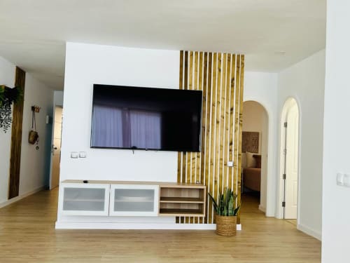 Modern living room with wall-mounted flat-screen TV, wooden slat partition, and white cabinetry in Arguineguín hotel suite