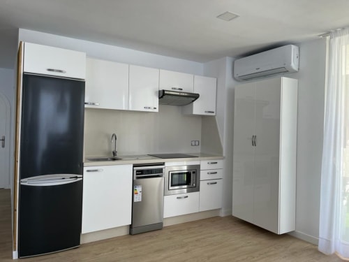 Modern kitchen with white cabinets, stainless steel appliances, and air conditioning in Arguineguín family suite