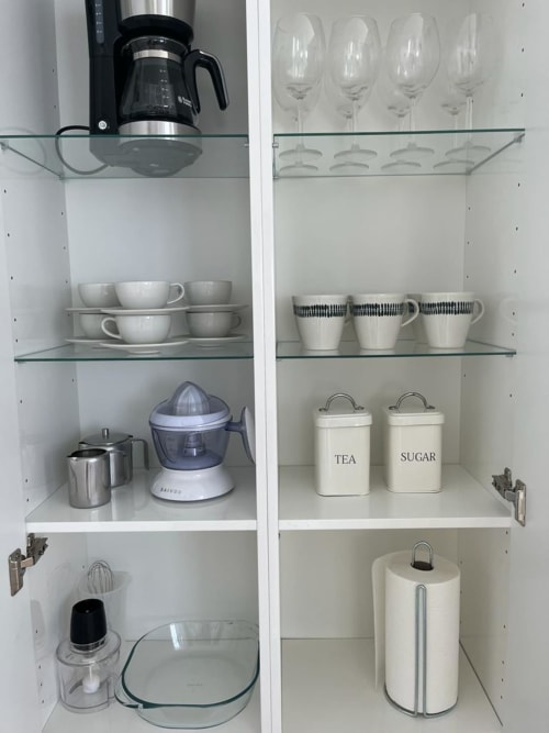 Organized kitchen cabinet in Sunset ocean view Family Suite 301, displaying glasses, mugs, appliances, and labeled tea and