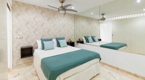 Modern 1-bedroom apartment bedroom with teal bedding, patterned wallpaper, and mirrored wall at Sunset ocean view hotel in