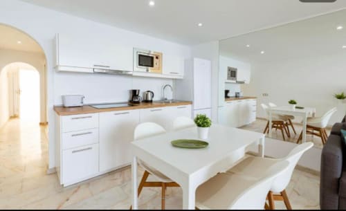 Modern white kitchen and dining area in Arguineguín apartment with sea views, wooden accents