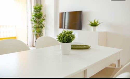 Modern dining area in Arguineguín apartment with white table, chairs, potted plants, and wall-mounted TV with sea view