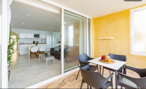 Modern 1-bedroom apartment in Arguineguín with dining area, yellow accent wall, and sea views through glass doors