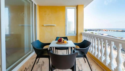 Modern balcony with sea view in Arguineguín apartment, featuring black chairs, white table with breakfast, yellow walls