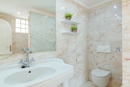 Modern bathroom in Arguineguín apartment with marble tiles, white sink, toilet, shelving with plants, and mirror lighting