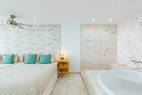 Sunset ocean view suite with marble bathroom, white bedding, turquoise pillows, and modern amenities in Arguineguín