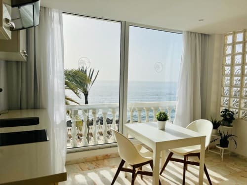 Studio apartment in Arguineguín with sea view balcony, white desk, chairs, and ocean vista through large windows