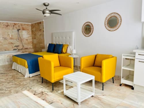 Modern studio apartment in Arguineguín with yellow chairs, white bed, marble flooring, and sea view amenities including TV