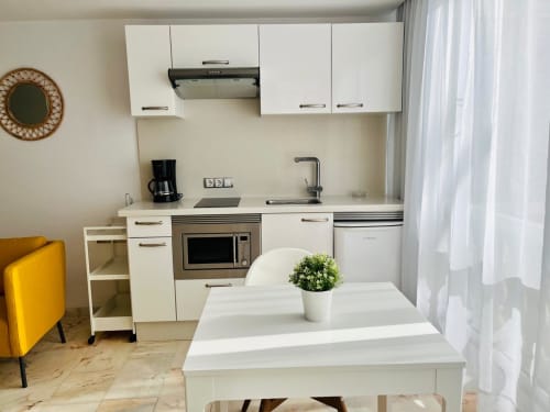 Modern white kitchen in Arguineguín studio apartment with island table, microwave, and sea view through window