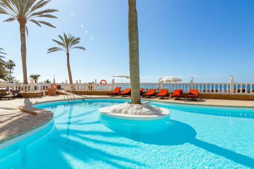 Luxury resort pool with turquoise water, palm trees, and ocean view in Arguineguín, Spain