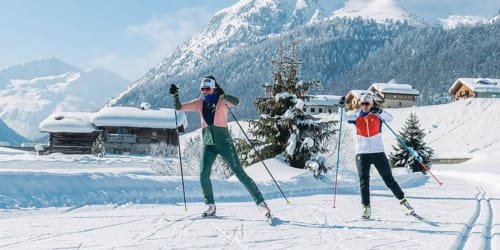 Due scialpinisti su pista innevata in Val di Livigno con villaggio alpino e chalet innevati sullo sfondo