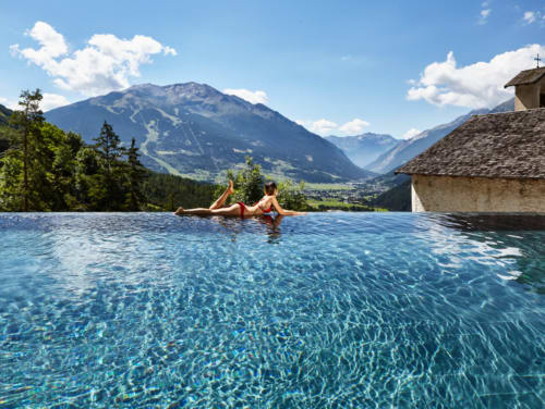 Woman relaxing in infinity pool overlooking Alpine mountains at Al Dos hotel in Livigno, Italy