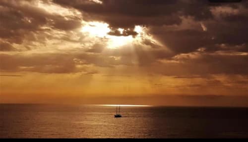 Segelboot bei Sonnenuntergang vor Arguineguín verankert mit dramatischem goldenem Himmel und Wolkendurchbrüchen