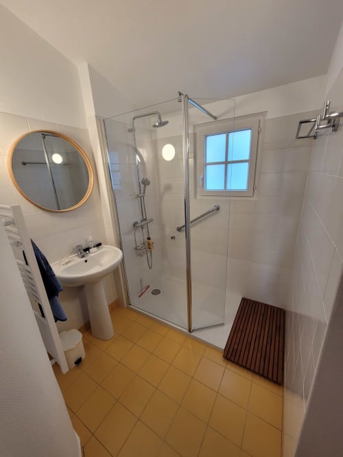 Salle de bain moderne avec douche à l'italienne, lavabo sur colonne, miroir rond et fenêtre du gîte Belle Île en Mer