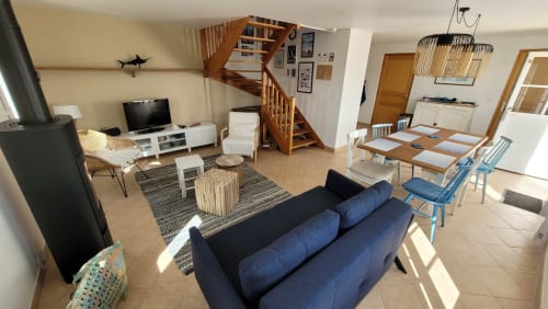 Spacieux séjour familial avec canapé bleu, table à manger, escalier en bois et vue sur le jardin près des plages de Belle Île