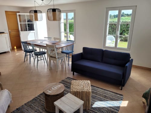 Séjour ouvert et lumineux du gîte Belle Île avec canapé bleu marine, table à manger, suspensions et vue sur le jardin