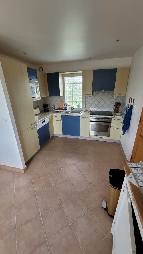 Cuisine moderne avec meubles crème et bleu marine, électroménagers en inox et dosseret carrelé dans un cottage à Belle-Île-en-Mer