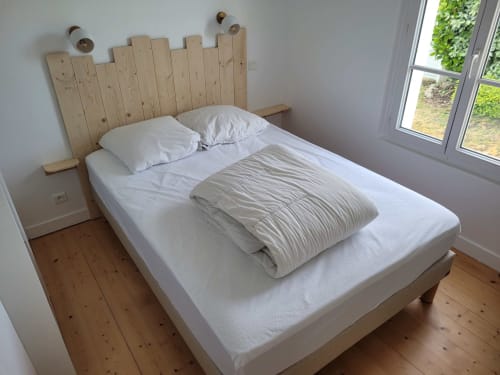 Chambre lumineuse avec tête de lit en bois, literie blanche et vue sur le jardin par grande fenêtre au gîte Loc'Maria à Belle Île