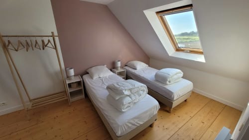 Chambre mansardée lumineuse avec deux lits simples, parquet bois et puits de lumière surplombant la campagne à la Maison de Locmaria