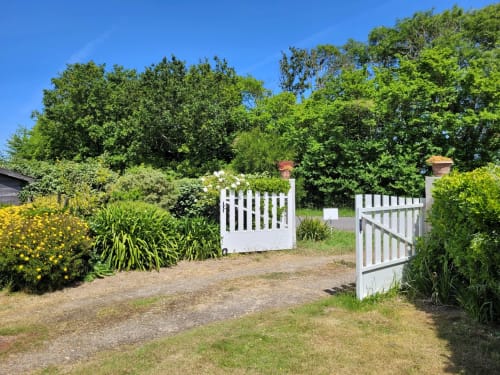 Portail blanc à claire-voie d'accès à la maison Belle Île avec jardins luxuriants et allées bordées d'arbres