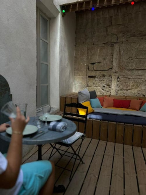 Colorful patio seating area at Mes à Moi Pézenas with brick walls, wooden deck, and vibrant pillows