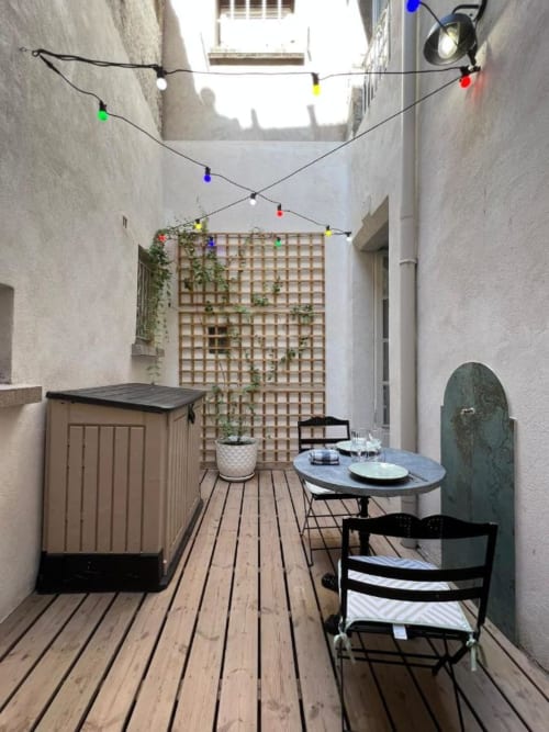 Narrow courtyard patio at Mes à Moi Pézenas with dining table, chairs, and colorful string lights overhead