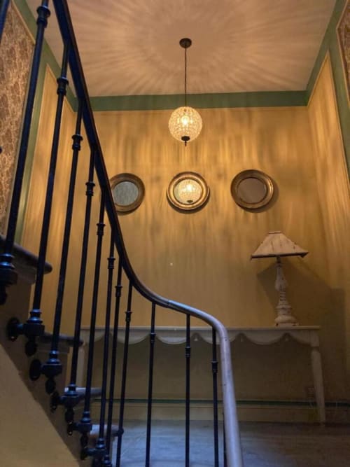 Élégant escalier du Mes à Moi Pézenas avec rampes en fer noir, murs jaunes, suspensions et appliques murales décoratives