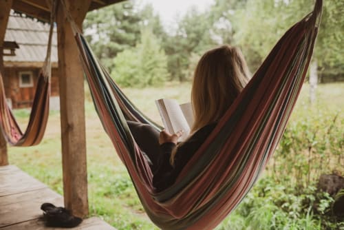 Femme lisant dans un hamac rayé à Lady Jule B&B à Sainte-Luce-sur-Loire, entourée d'arbres et de vue sur le jardin