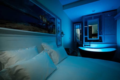 Modern blue-lit bedroom and bathroom at Mes à Moi Pézenas B&B in France with bed, pillows, and contemporary bathtub.