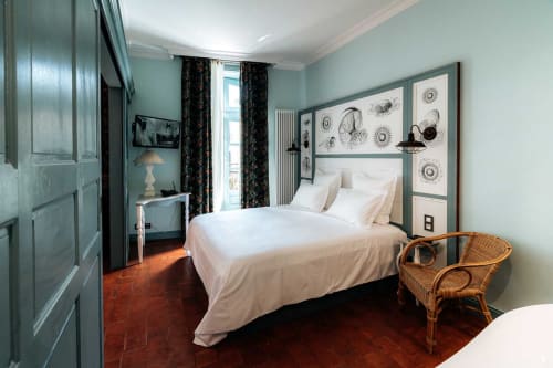 Chambre élégante à Mes à Moi Pézenas aux murs bleu pâle, literie blanche, carrelage terre cuite et œuvres botaniques