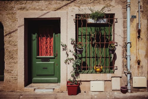 Entrée charmante du gîte de Pézenas avec porte verte, grille en fer forgé, plantes en pots et façade en pierre rustique