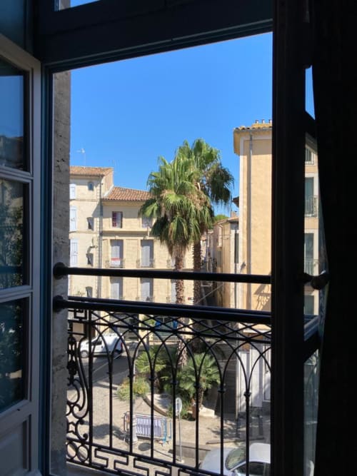 Vue depuis le balcon de Mes à Moi Pézenas sur la rue du village français avec palmier et bâtiments historiques