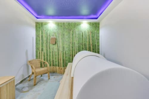 Espace bien-être du spa Mes à Moi Pézenas avec mur en bambou, lit de massage, fauteuil en rotin et éclairage plafond violet