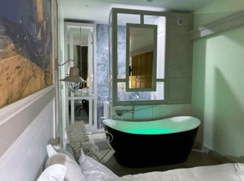 Salle de bain contemporaine au Mes à Moi Pézenas avec baignoire îlot noire, éclairage d'accent vert et vanité épurée
