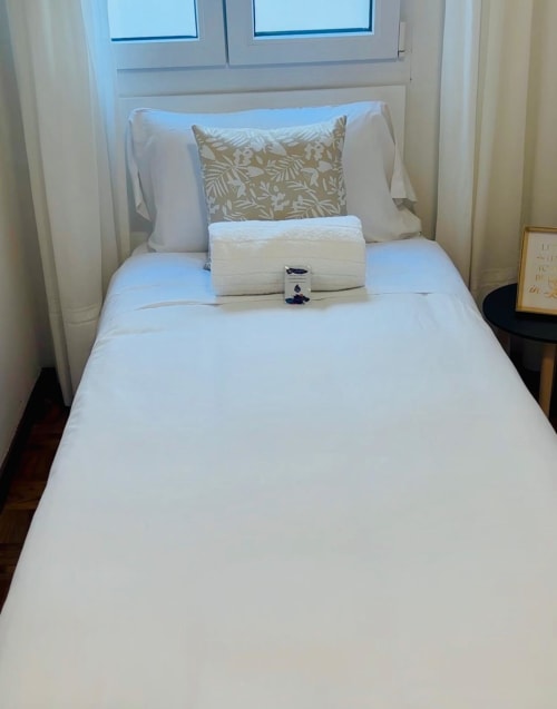 Dormitorio moderno y limpio en apartamento Holibai de Baiona con ropa de cama blanca, almohadas decorativas, toallas enrolladas y ventanas