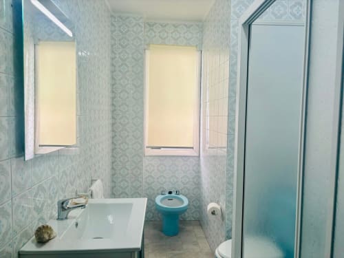 Baño moderno del apartamento Breixo en Baiona con lavabo blanco, inodoro turquesa, ducha y paredes con azulejos decorativos