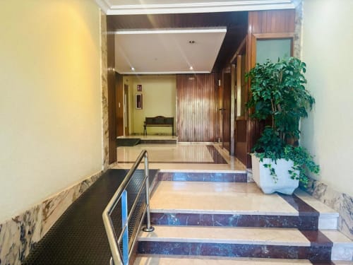 Entrada moderna de apartamento con escaleras de mármol, barandillas metálicas y plantas en macetas en Holibai, Baiona, España
