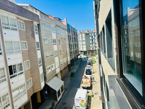 Vista de calle estrecha entre edificios residenciales en Baiona con coches aparcados y cielo despejado, mostrando un entorno urbano de apartamentos
