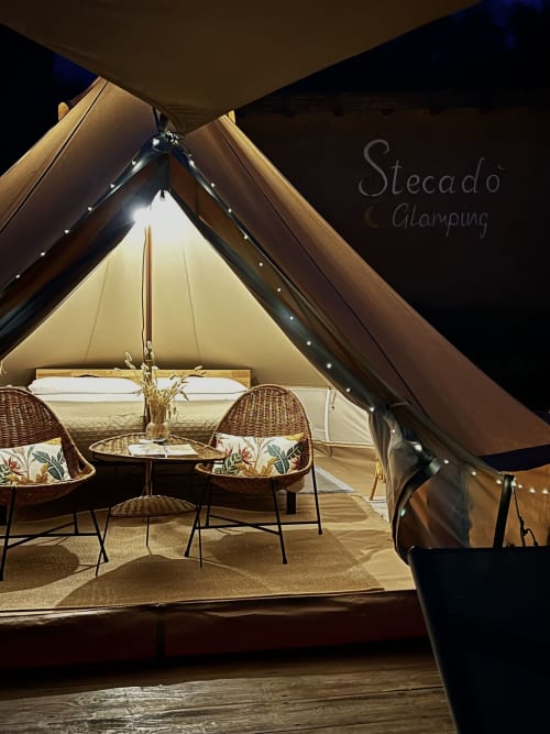 Tente de glamping luxueuse à Stecadò avec fauteuils en osier, guirlandes lumineuses et vue sur le jardin à Dolceacqua