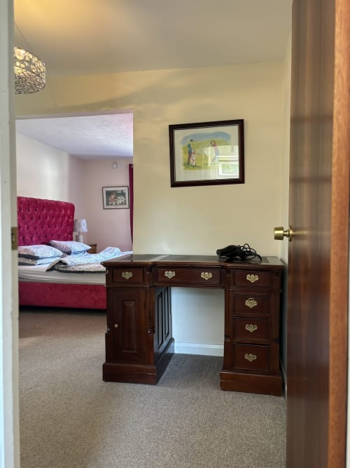 Spacious bedroom with dark wood desk, burgundy bed, and framed artwork at England Furnished Homes in High Wycombe