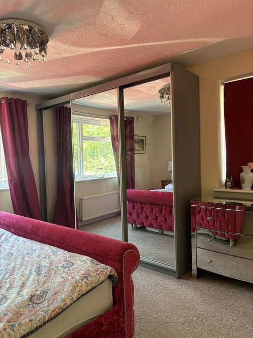 Luxe bedroom with mirrored wardrobe, burgundy upholstered bed, pink ceiling, garden view window at England Furnished Homes