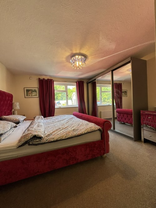 Luxe bedroom with burgundy upholstered bed, mirrored wardrobes, red curtains, and garden views in High Wycombe villa