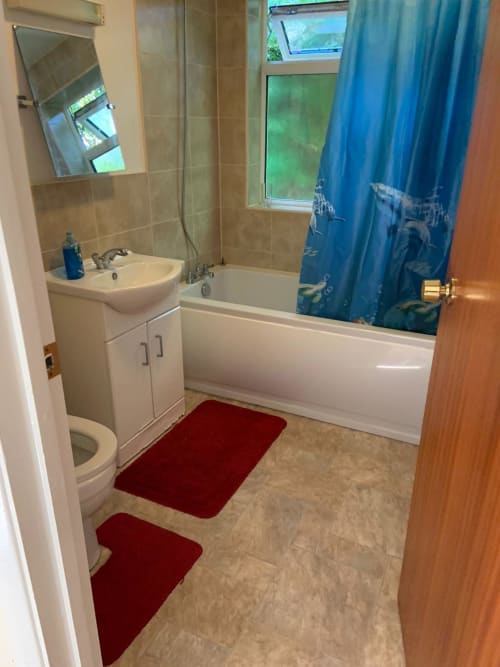 Modern bathroom with white suite, sink vanity, bathtub with blue shower curtain, red bath mats, and tiled walls in High
