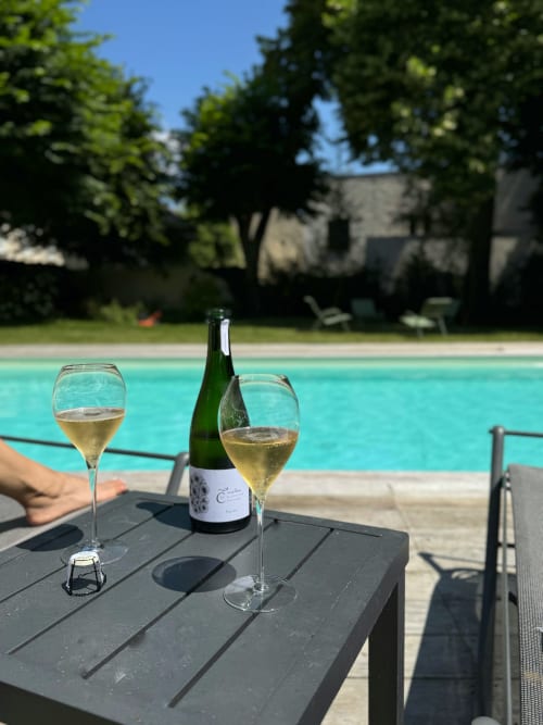 Two glasses of white wine and bottle by turquoise pool at Le château d'Hermonville, France